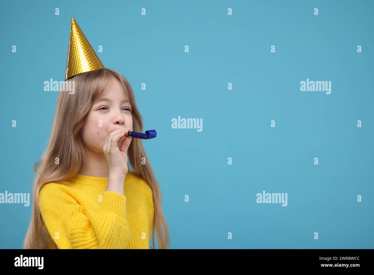 Cute little girl in party hat with blower on light blue background ...