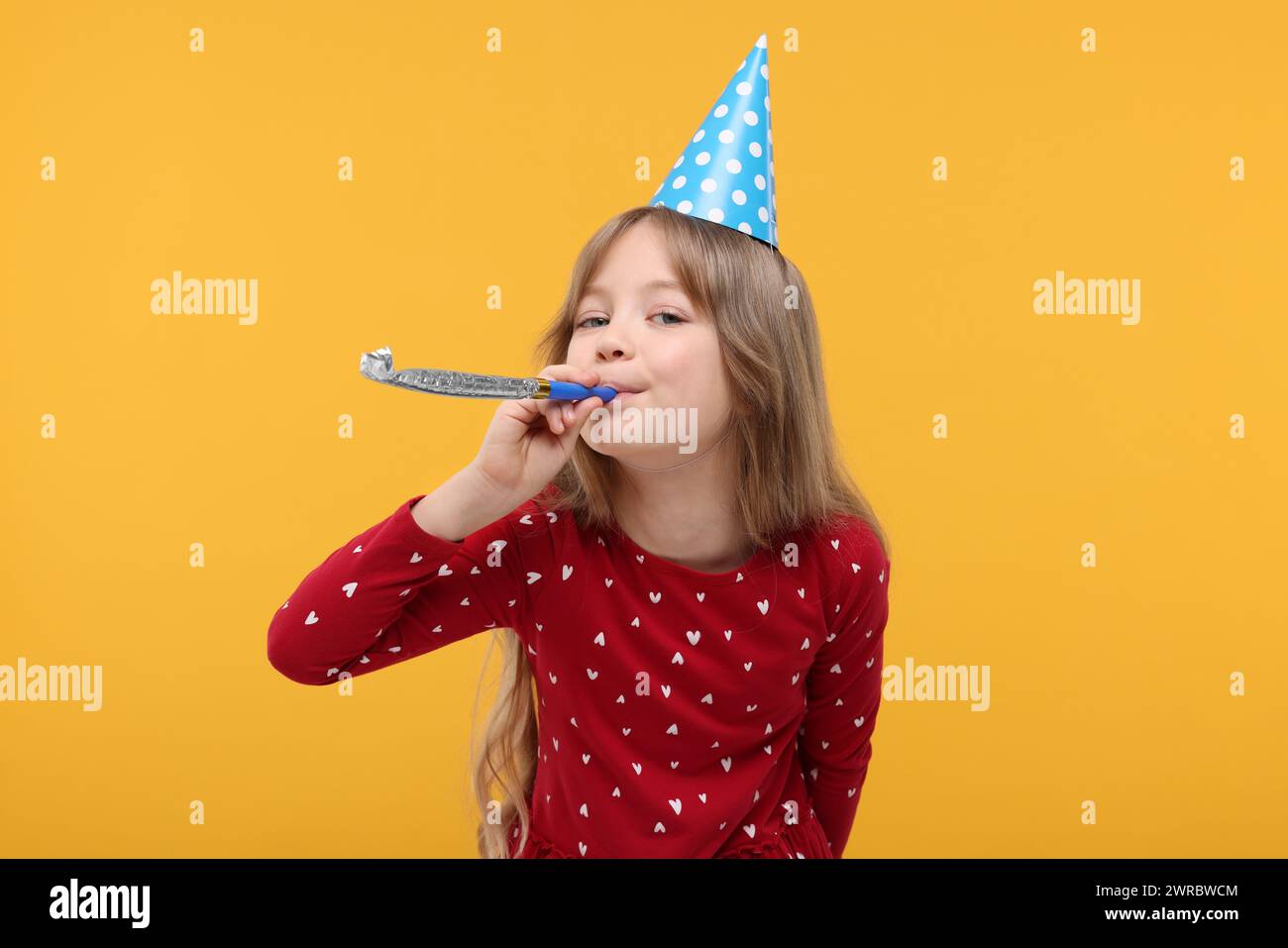 Cute little girl in party hat with blower on yellow background Stock ...