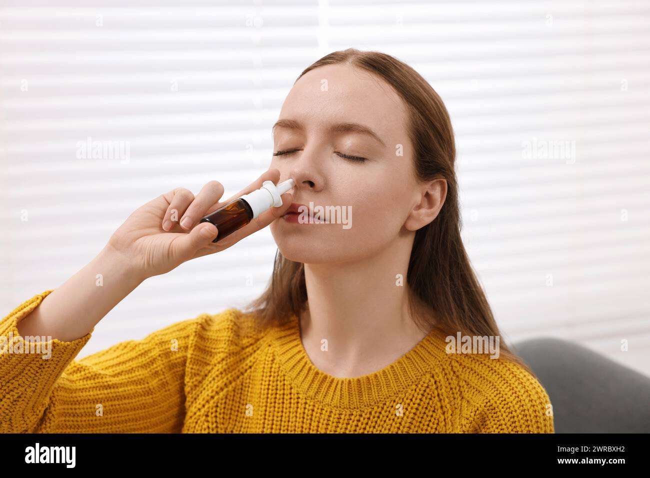 Medical drops. Young woman using nasal spray indoors Stock Photo