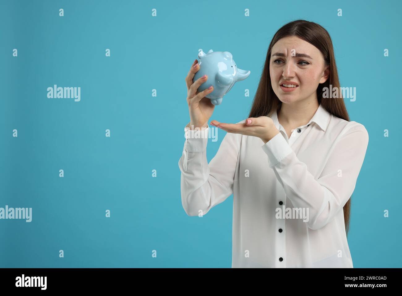 Sad woman with piggy bank on light blue background, space for text ...