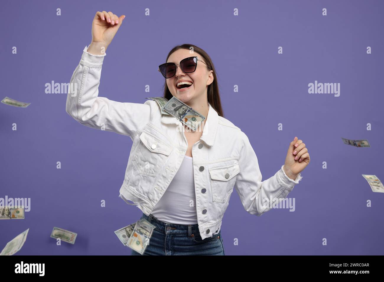 Happy woman under money shower on purple background Stock Photo