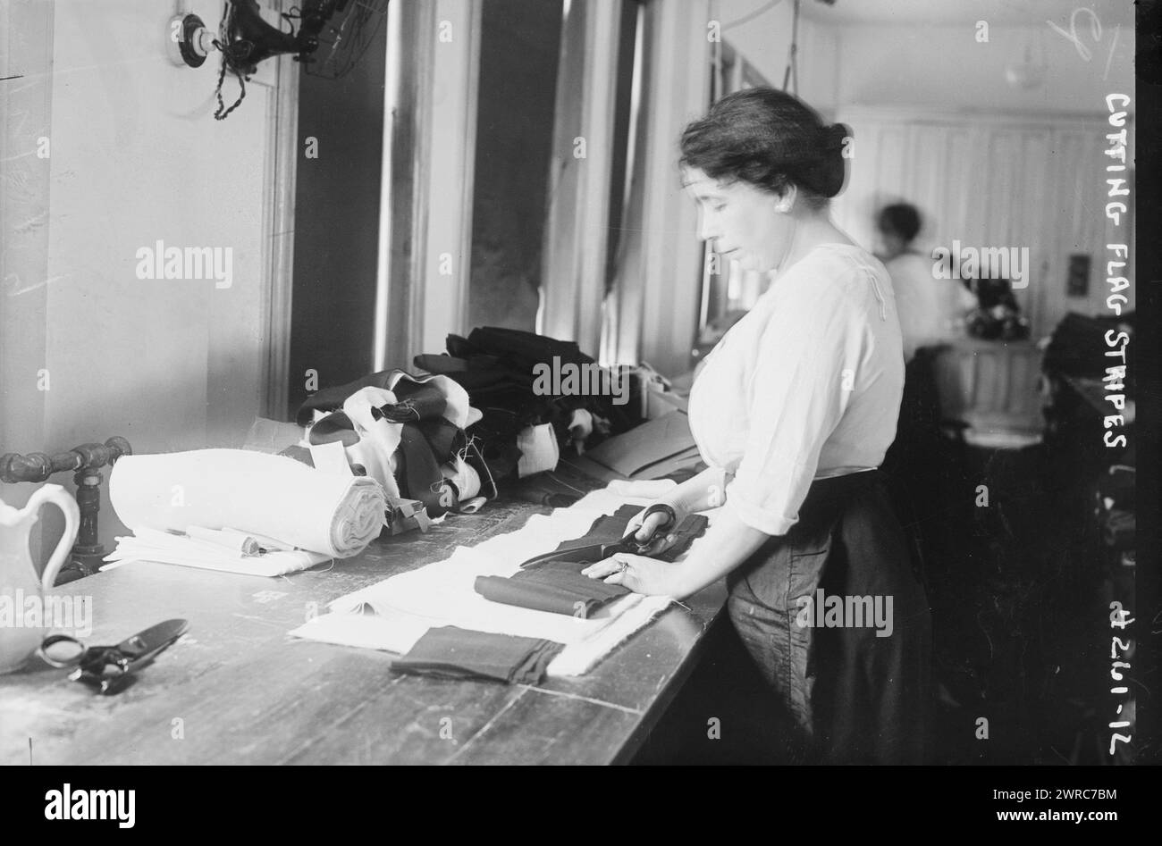 Cutting flag stripes, Photograph shows women cutting stripes for American flags with scissors at the Brooklyn Navy Yard, Brooklyn, New York., 1917 July 7, Glass negatives, 1 negative: glass Stock Photo