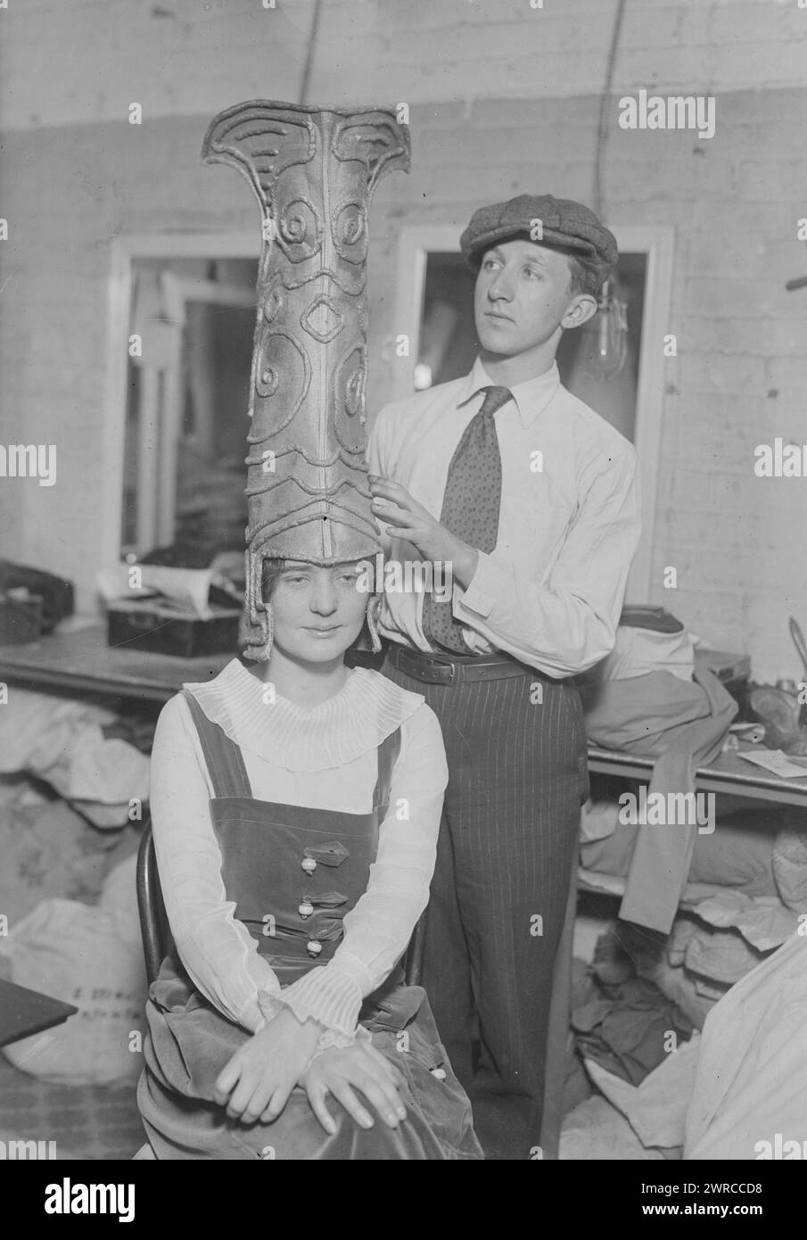 Margaret Mower, Photograph shows young man putting a tall headdress on actress Margaret Mower, possibly for a performance of 'The Laughter of the Gods', back stage in a theater., 1919, Glass negatives, 1 negative: glass Stock Photo