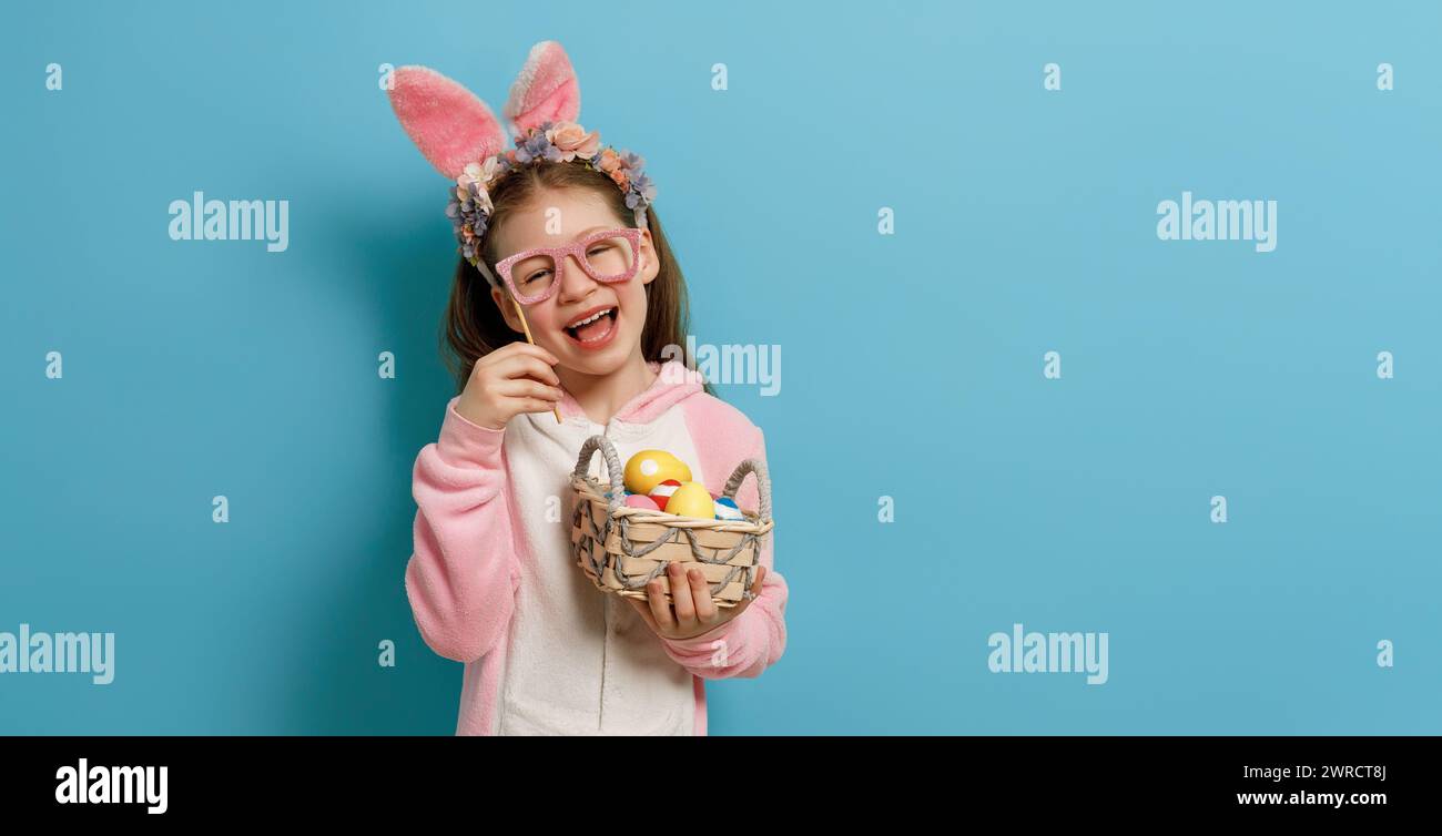 Cute little child wearing bunny ears on Easter day. Girl with painted eggs. Stock Photo