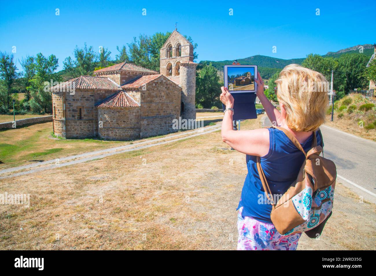 Woman taking photos of Romanesque church with a tablet. San Salvador de Cantamuda, Palencia province, Castilla Leon, Spain. Stock Photo