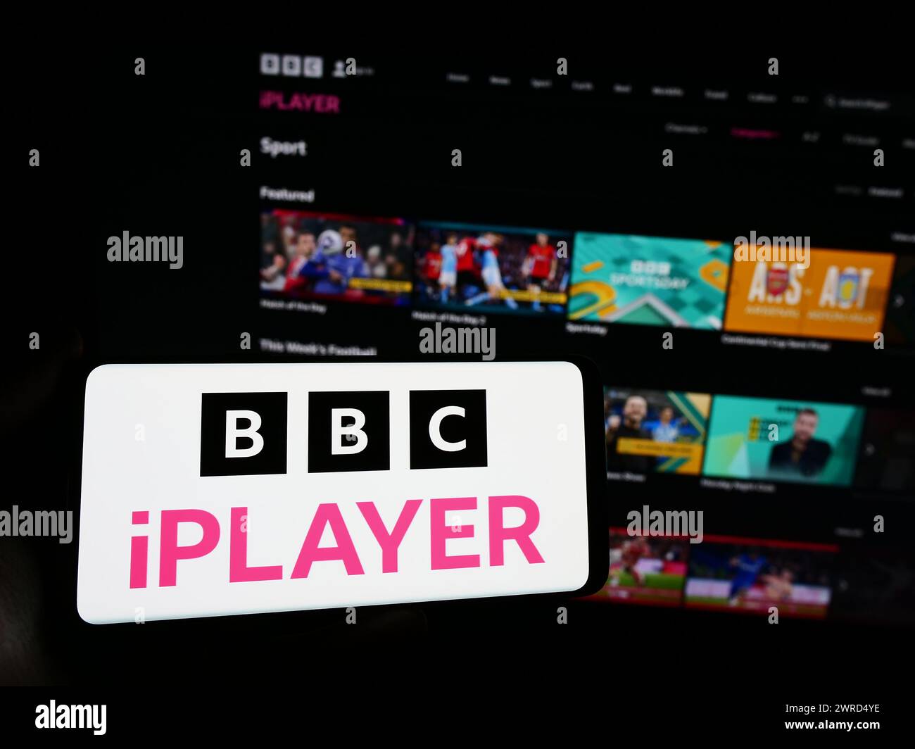 Person holding smartphone with logo of British video on demand service BBC iPlayer in front of website. Focus on phone display. Stock Photo