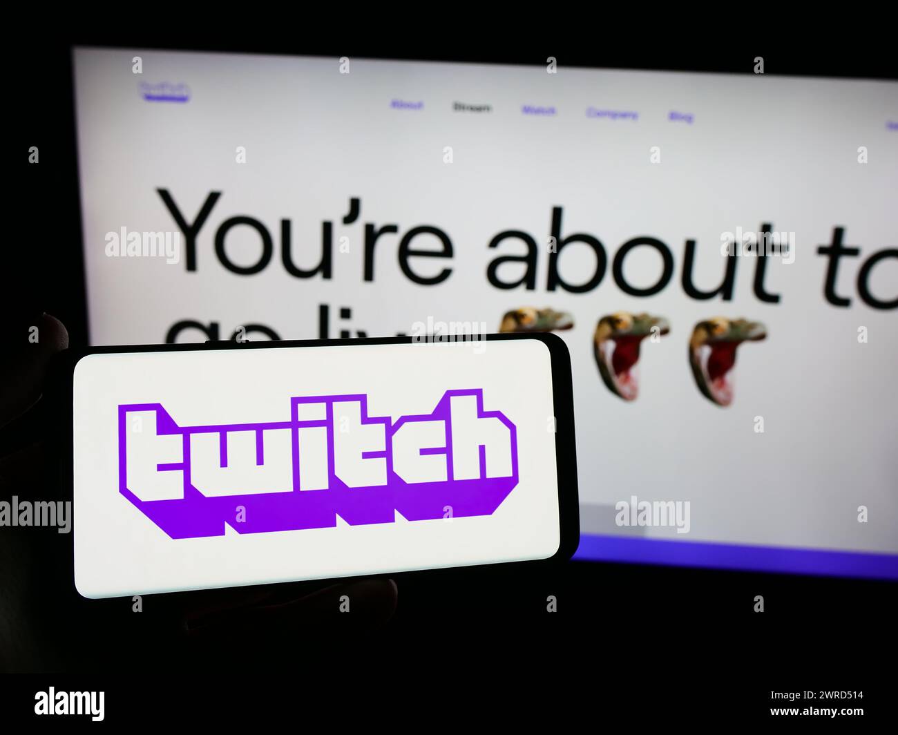 Person holding smartphone with logo of US live streaming company Twitch Interactive Inc. in front of website. Focus on phone display. Stock Photo