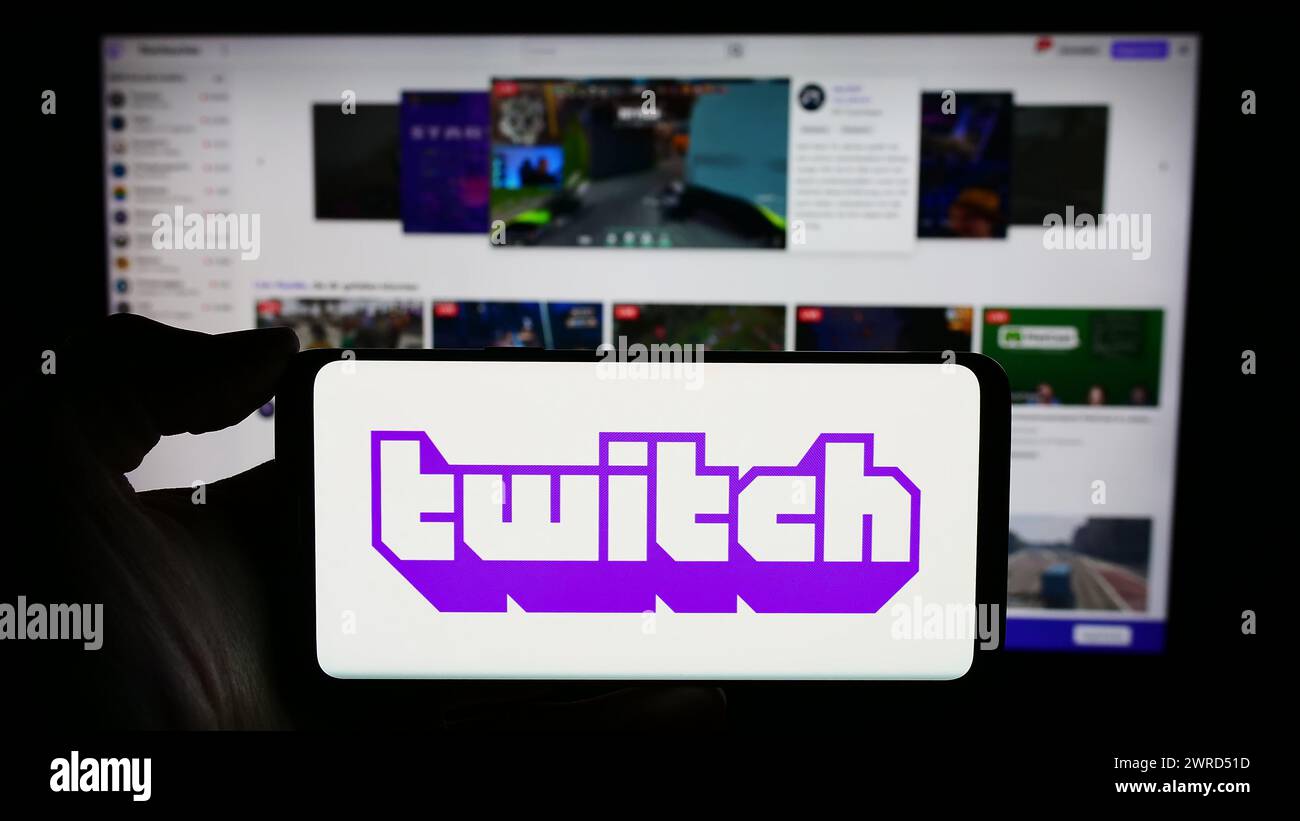 Person holding cellphone with logo of US live streaming company Twitch Interactive Inc. in front of business webpage. Focus on phone display. Stock Photo