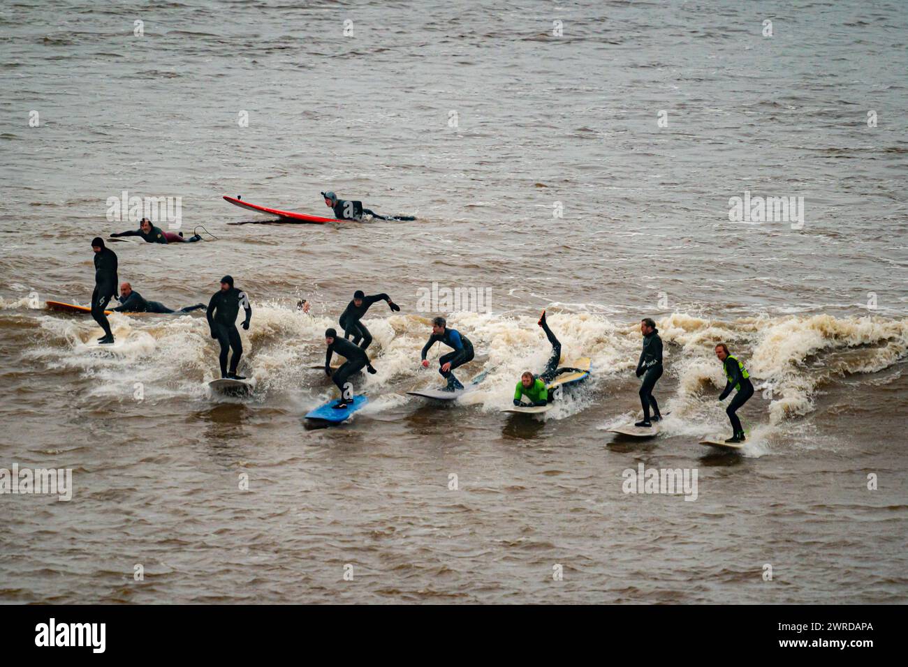 Surfers ride the first a 'five-star' Severn Bore of 2024 at Newnham, Gloucestershire. The bore, a large surge wave, is formed in the estuary of the River Severn, where the tidal range is the second highest in the world, and is caused when the incoming tide is funneled into an increasingly narrow channel against the current of the river. Picture date: Tuesday March 12, 2024. Stock Photo