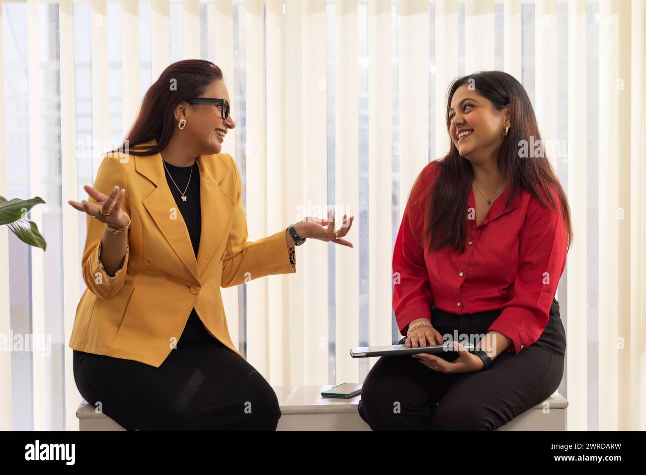Portrait of two businesswoman sitting on a bench and having a casual discussion in office Stock Photo