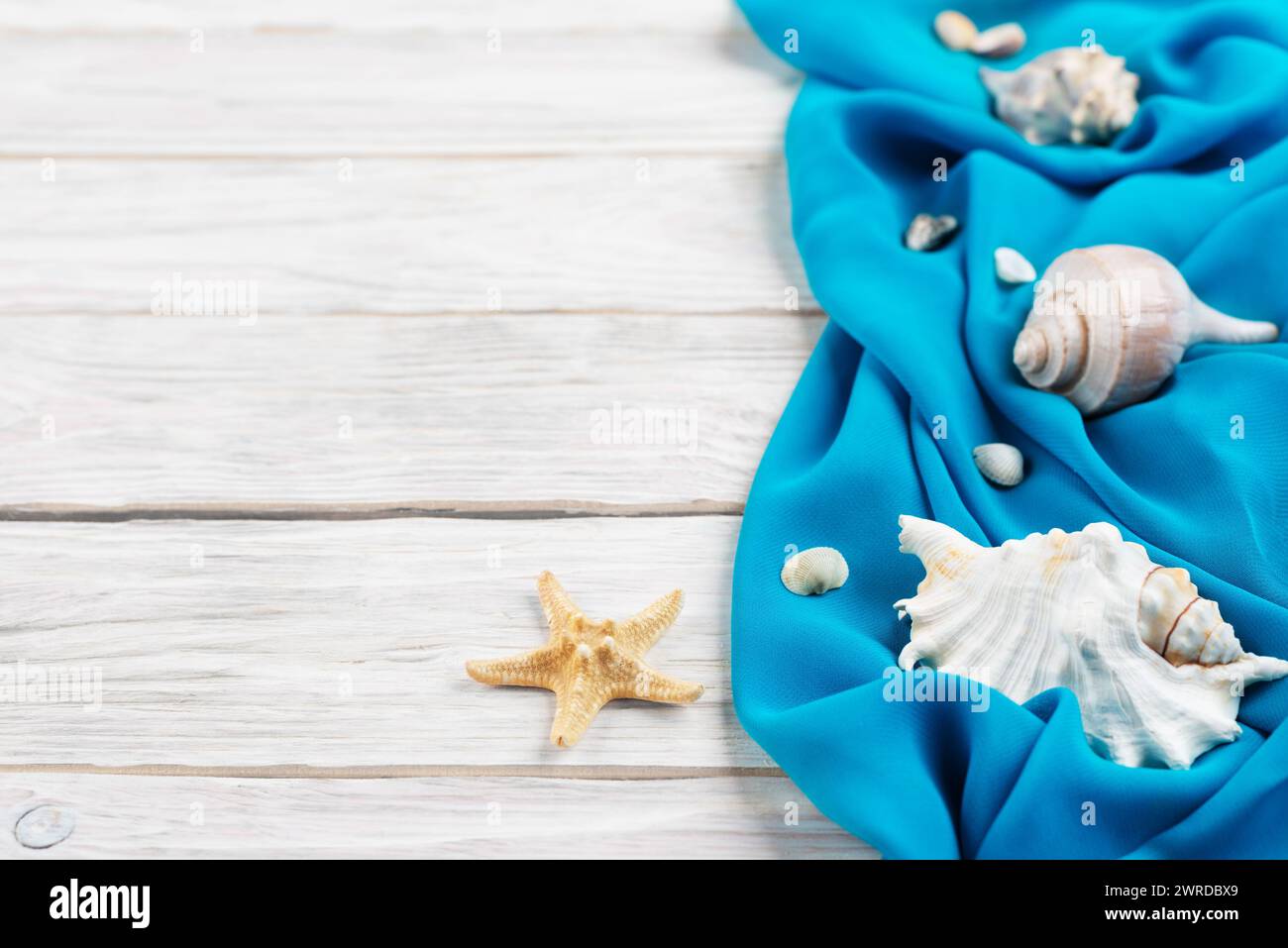 Seashells, blue fabric and starfish on white planks vacation planning background flat lay with copy-space Stock Photo