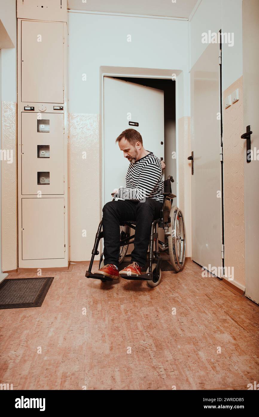 Disabled man on wheel chair leaving his apartment in prefab house Stock Photo