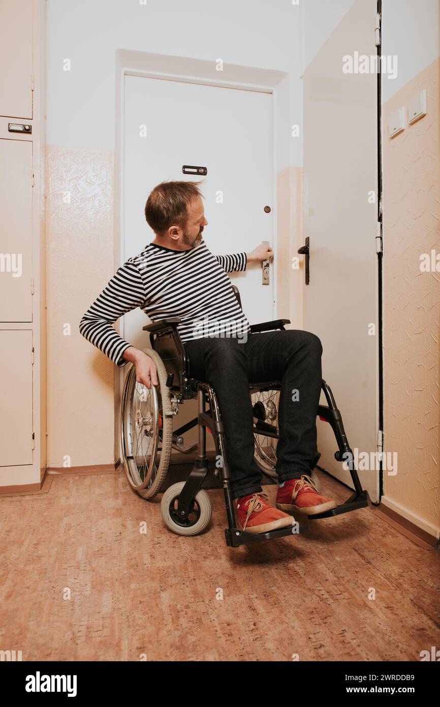 Disabled man on wheel chair leaving his apartment in prefab house Stock Photo