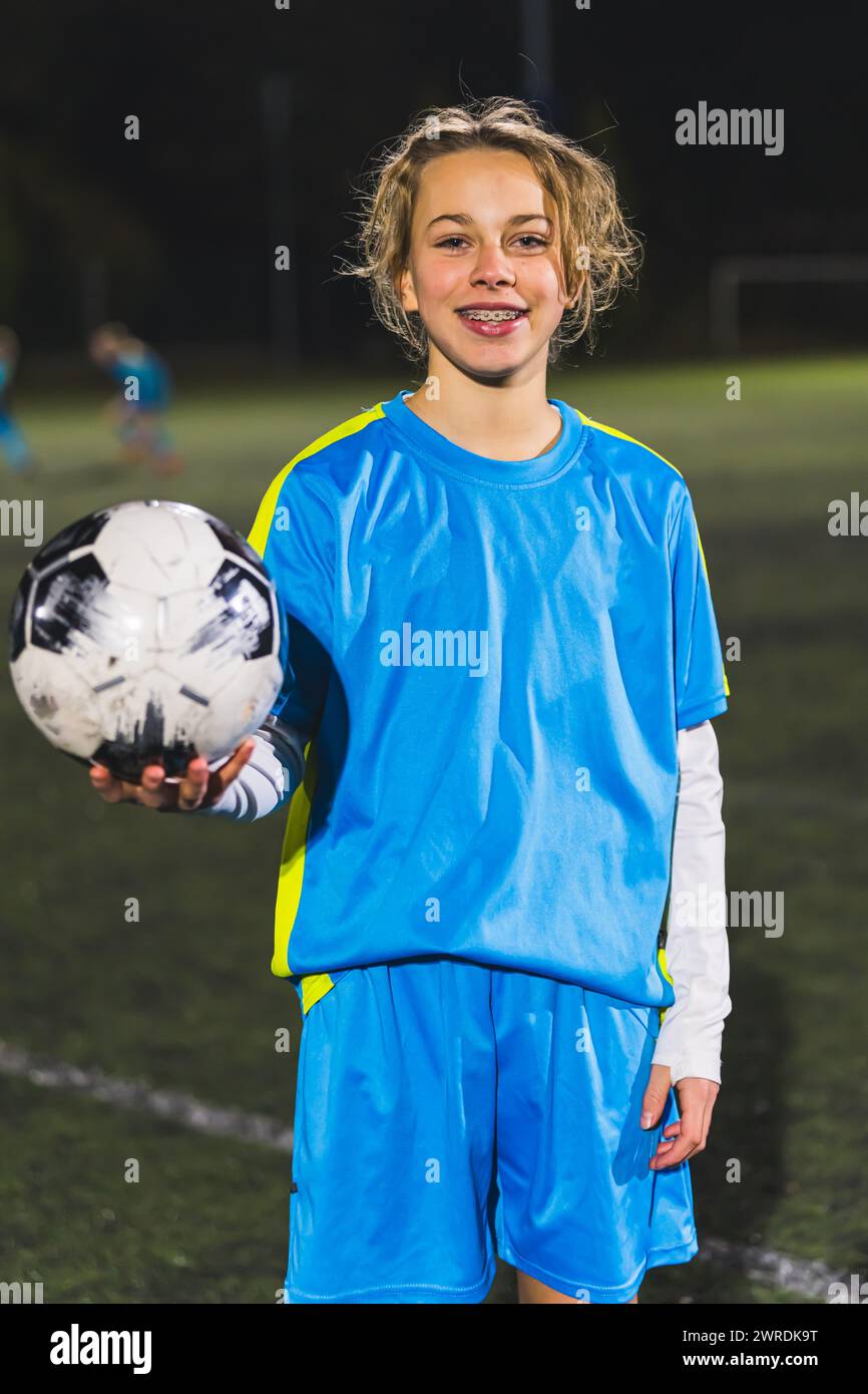cheerful and happy little girl in a blue uniform holding a soccer ball and taking a photo. High quality photo Stock Photo