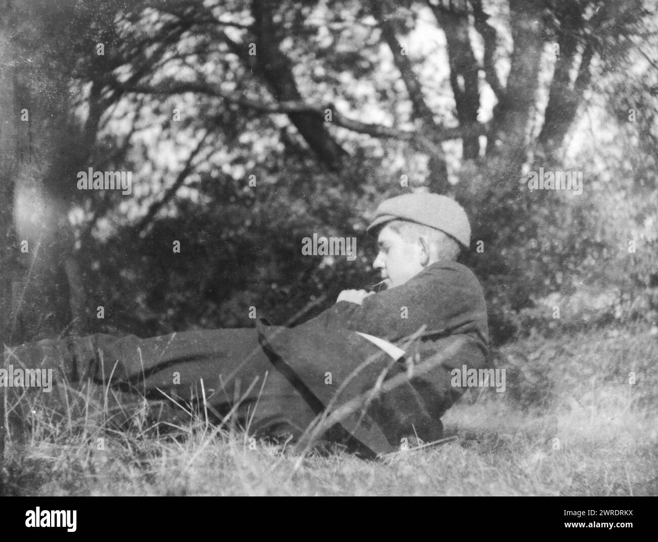 Image of pensive young man lying in countryside field with trees c 1910-1920 Stock Photo