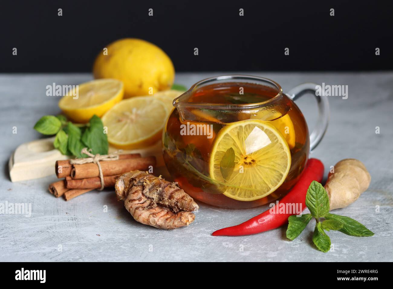 Glass teapot with ginger tea, lemon, turmeric root and mint on grey background with space for text. Cold and flu season concept. Stock Photo