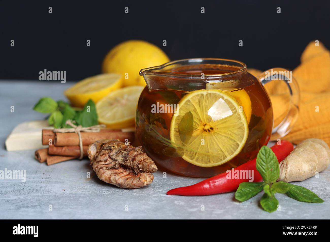 Glass teapot with ginger tea, lemon, turmeric root and mint on grey background with space for text. Cold and flu season concept. Stock Photo