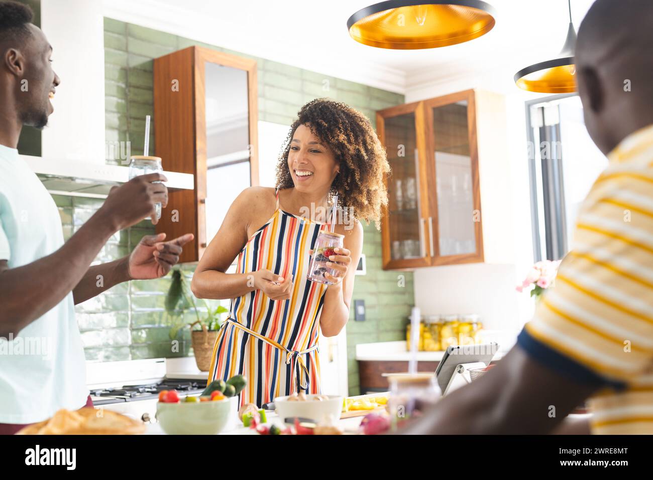 Diverse friends of young African American men and a biracial woman enjoy drinks in a sunny kitchen Stock Photo