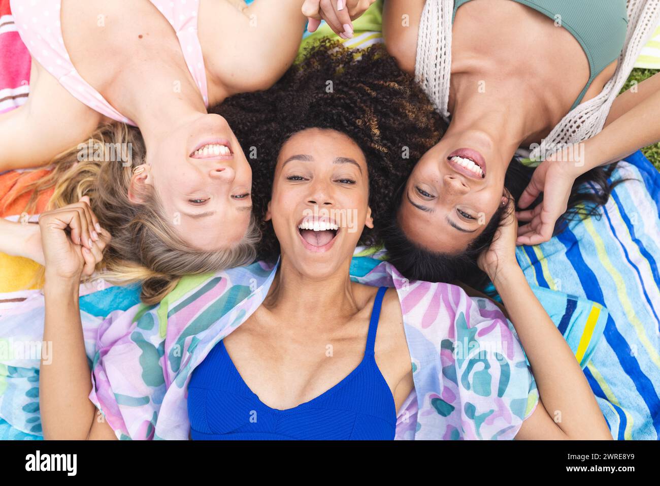 Three women are lying on a colorful blanket, heads together, smiling joyfully Stock Photo