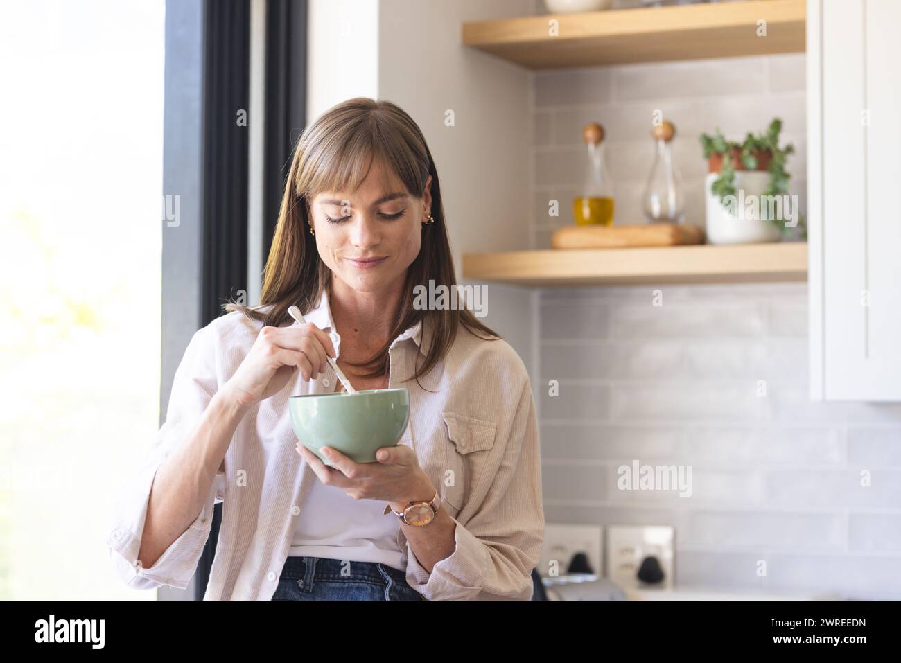 Caucasian woman enjoys a meal in a bright kitchen setting Stock Photo