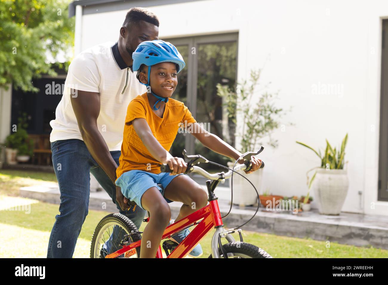 African American father teaches his son to ride a bike in a sunny backyard Stock Photo