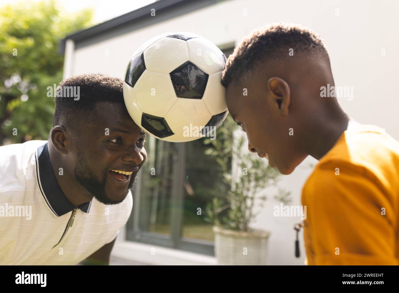 African American father and son play with a soccer ball outdoors in the backyard Stock Photo