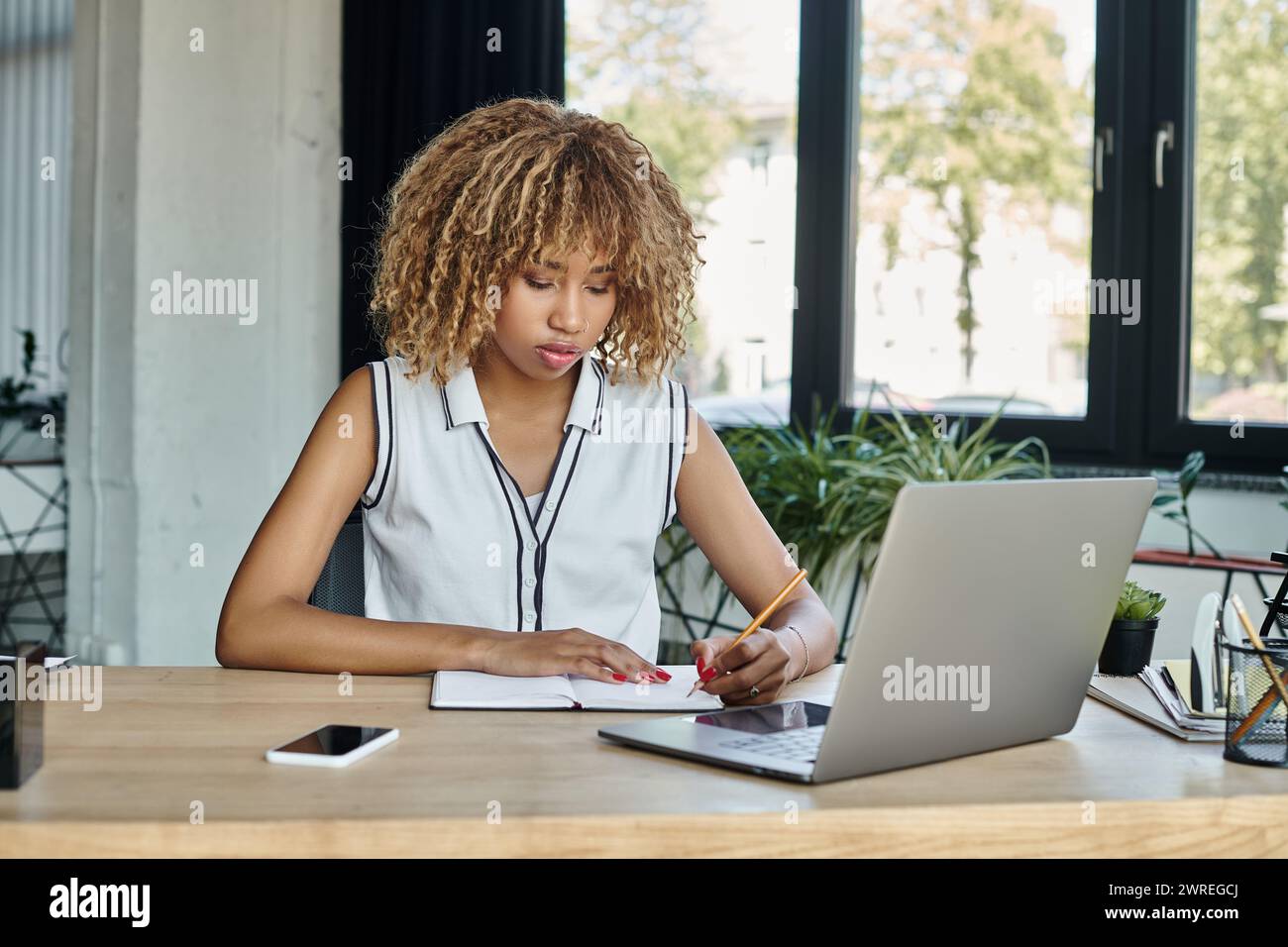 Concentrated african american businesswoman taking notes beside laptop ...