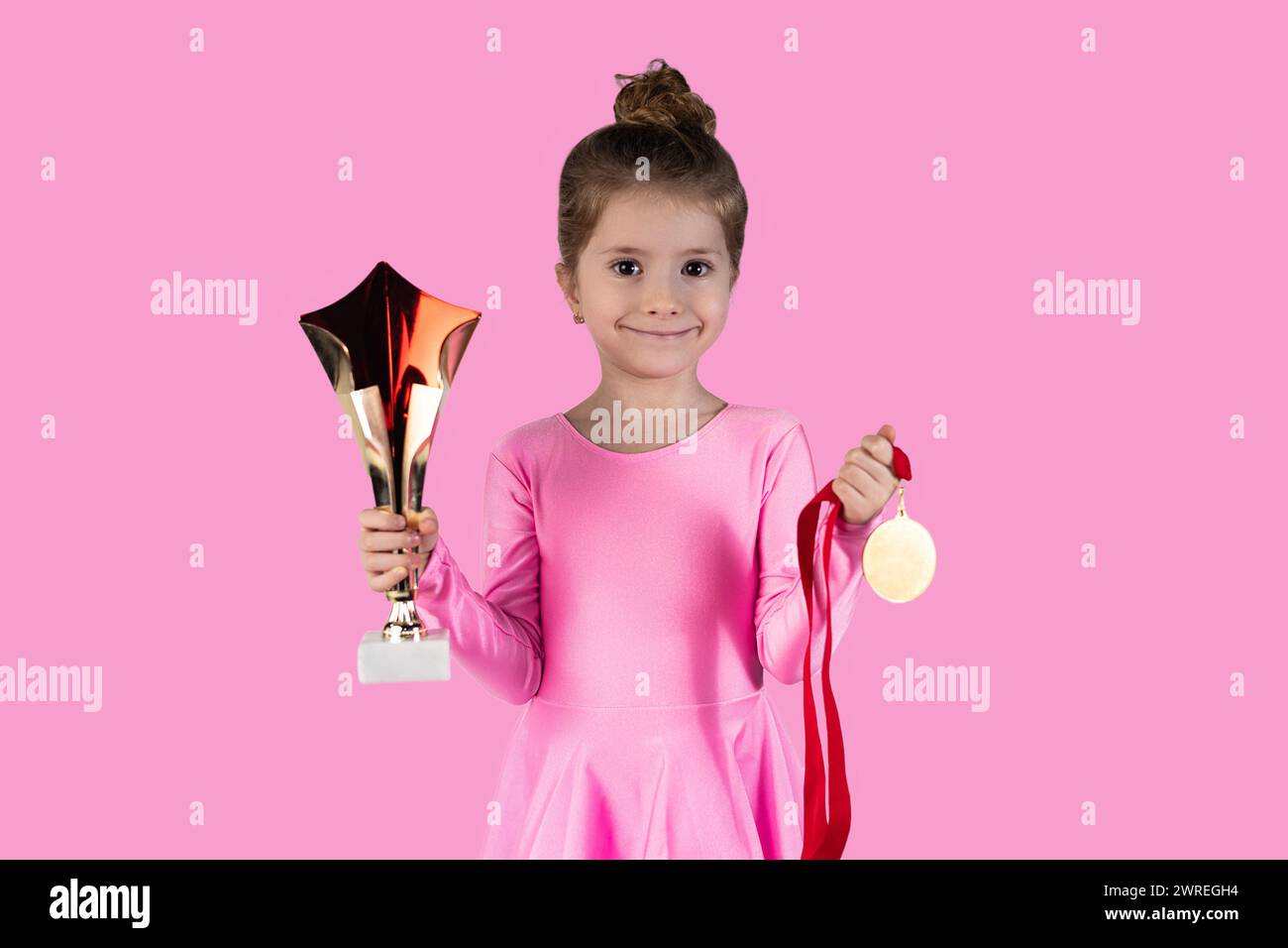 Joyful sports girl celebrating victory isolated on pink background wearing gold medal showing trophy she won. High quality photo Stock Photo