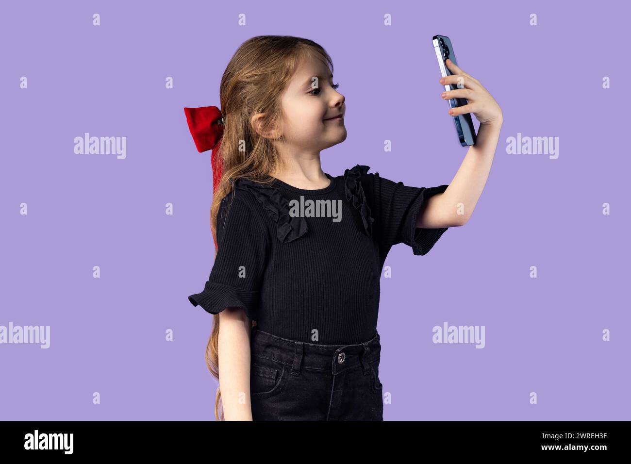 Portrait of a happy little girl wearing a black t-shirt, video chatting with her friends with the help of social networks on the mobile phone, using m Stock Photo
