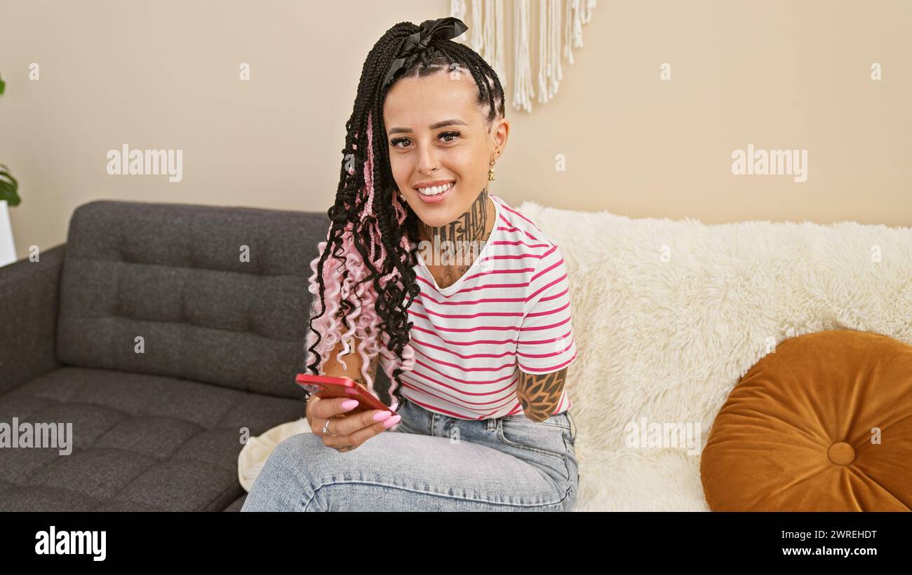 Cheerful hispanic amputee woman joyfully using smartphone at home, sitting on sofa with a positive, expressive smile Stock Photo