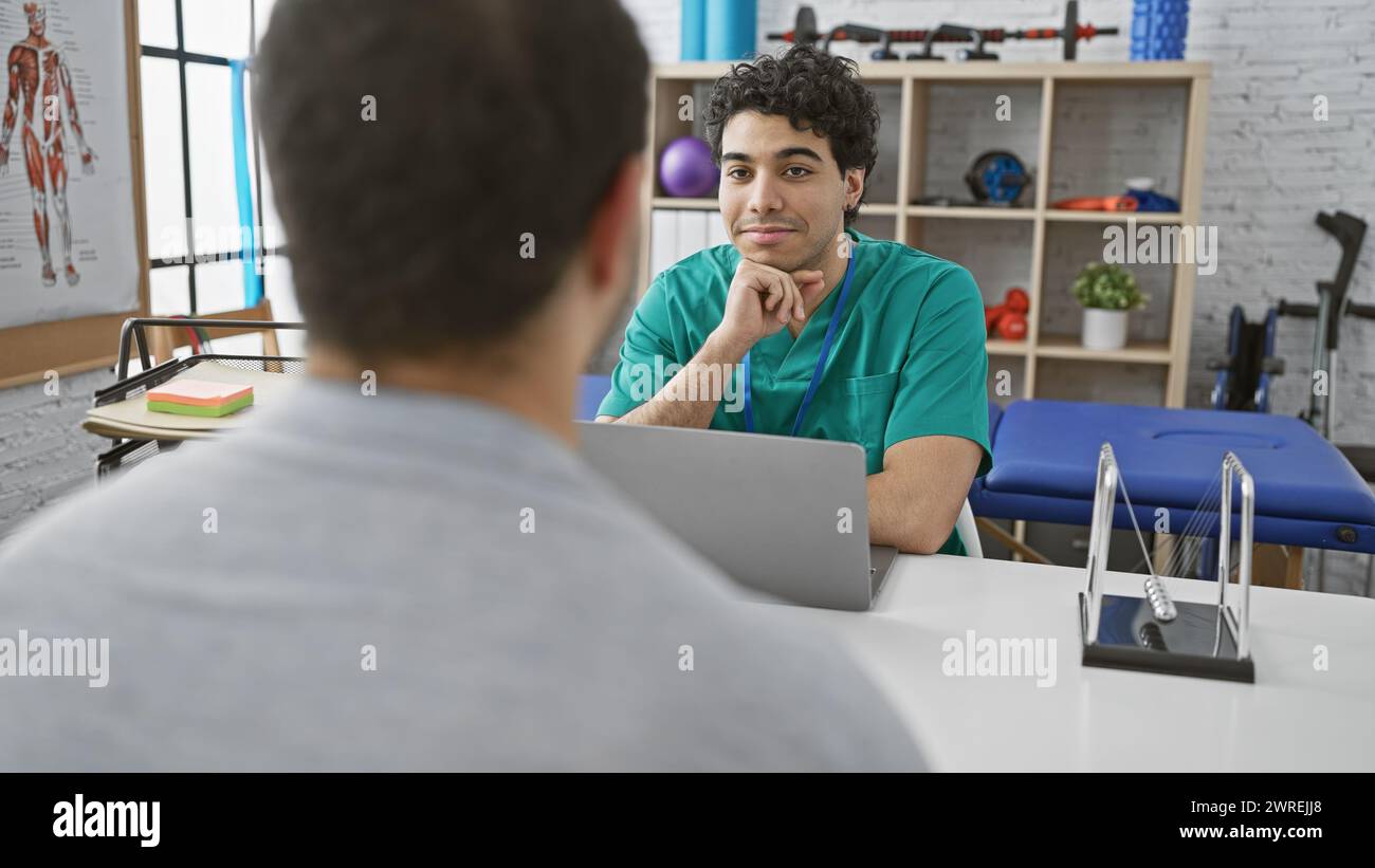 A male physiotherapist in a clinic listens attentively to a male patient during a rehabilitation session. Stock Photo