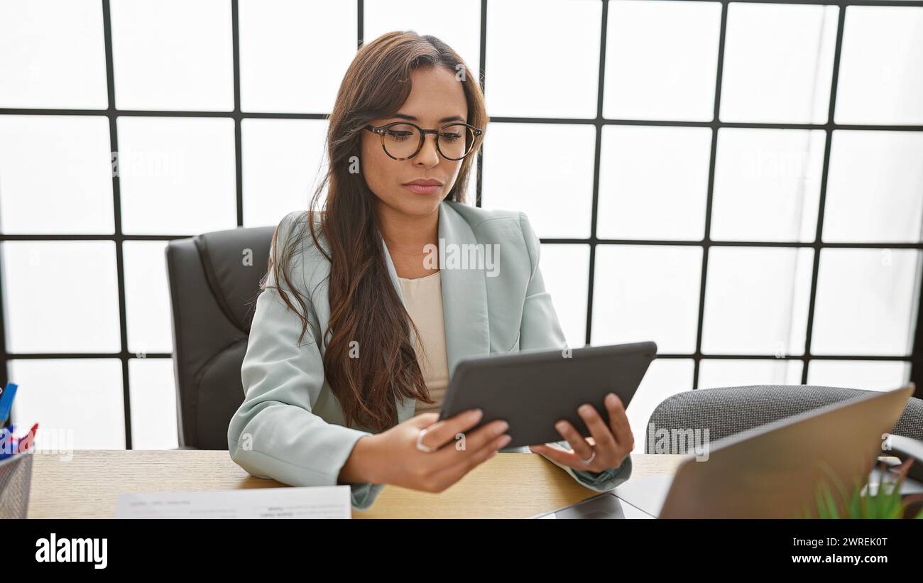 Serious and successful young hispanic woman works elegantly with laptop and touchpad at her office desk as the boss. Stock Photo