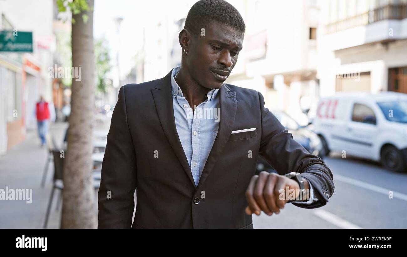 Handsome african man in suit checking time on watch in a city street ...