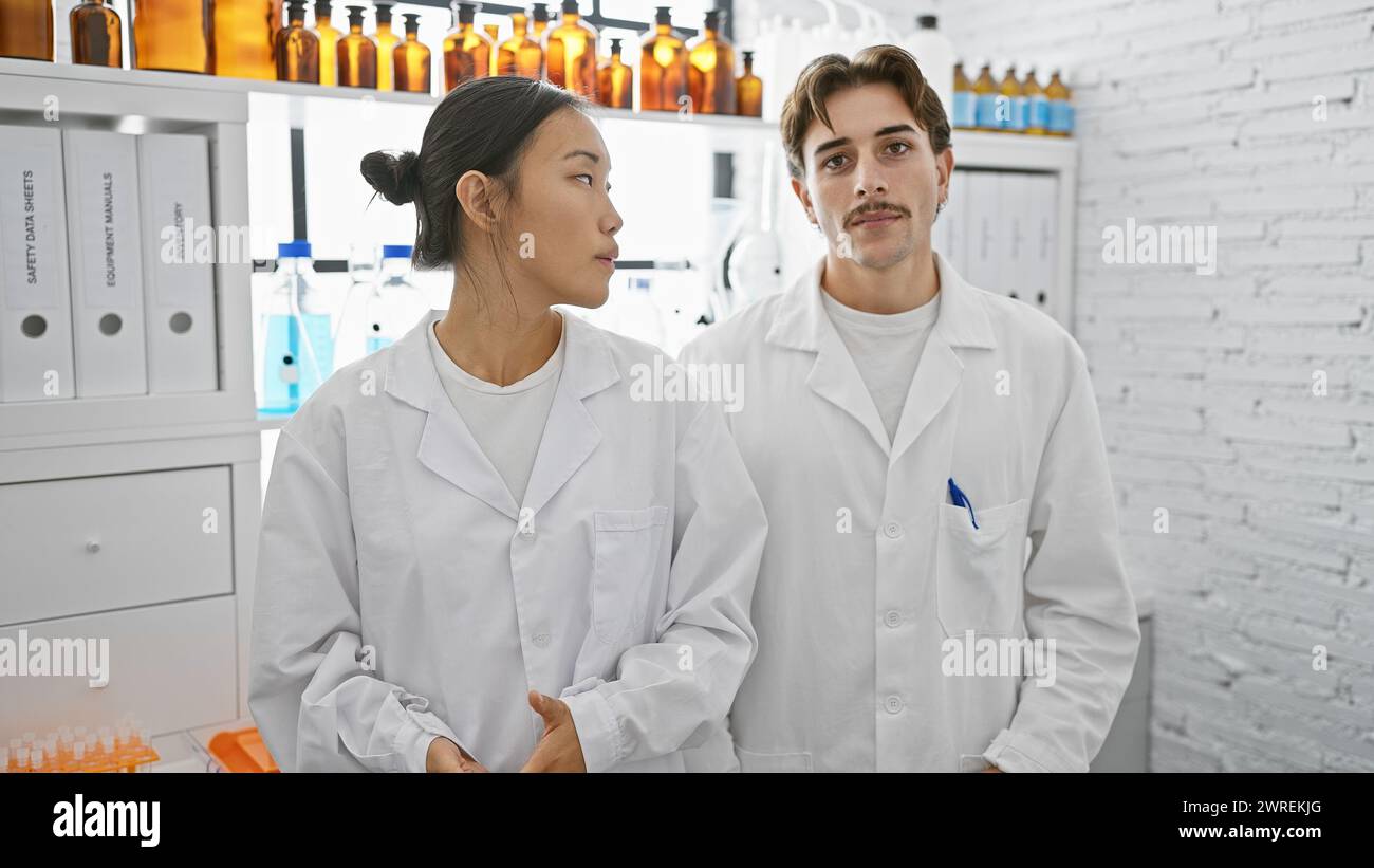 A man and woman in white lab coats stand in a laboratory adorned with ...