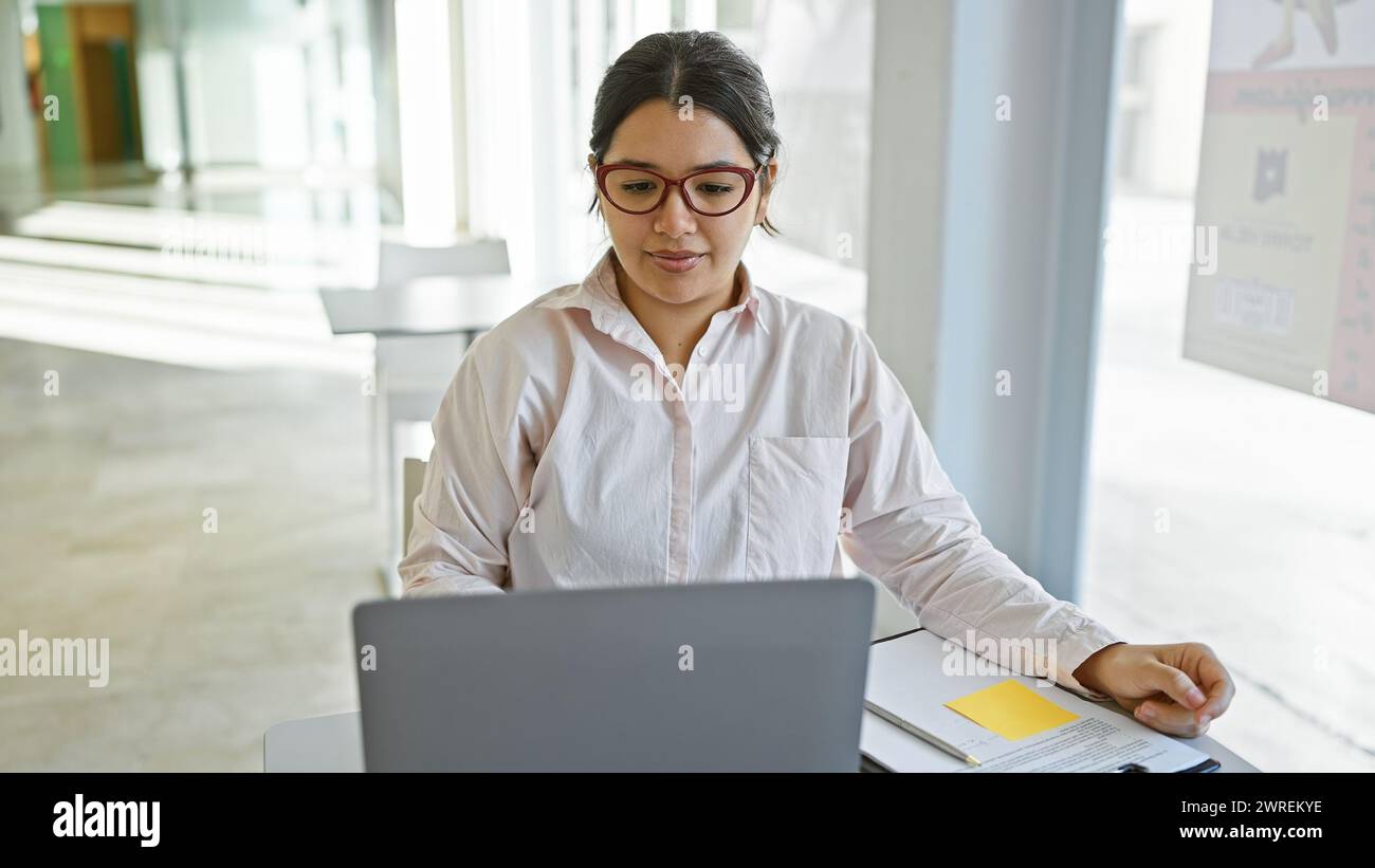 A focused hispanic woman works on her laptop in a bright modern office ...