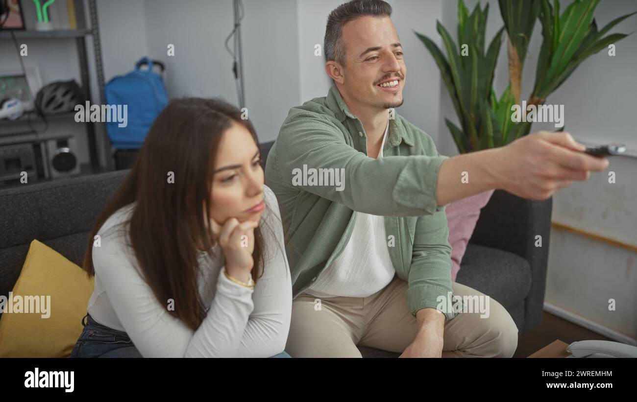 An engaged man and bored woman sitting on a couch in a modern living room, home entertainment. Stock Photo