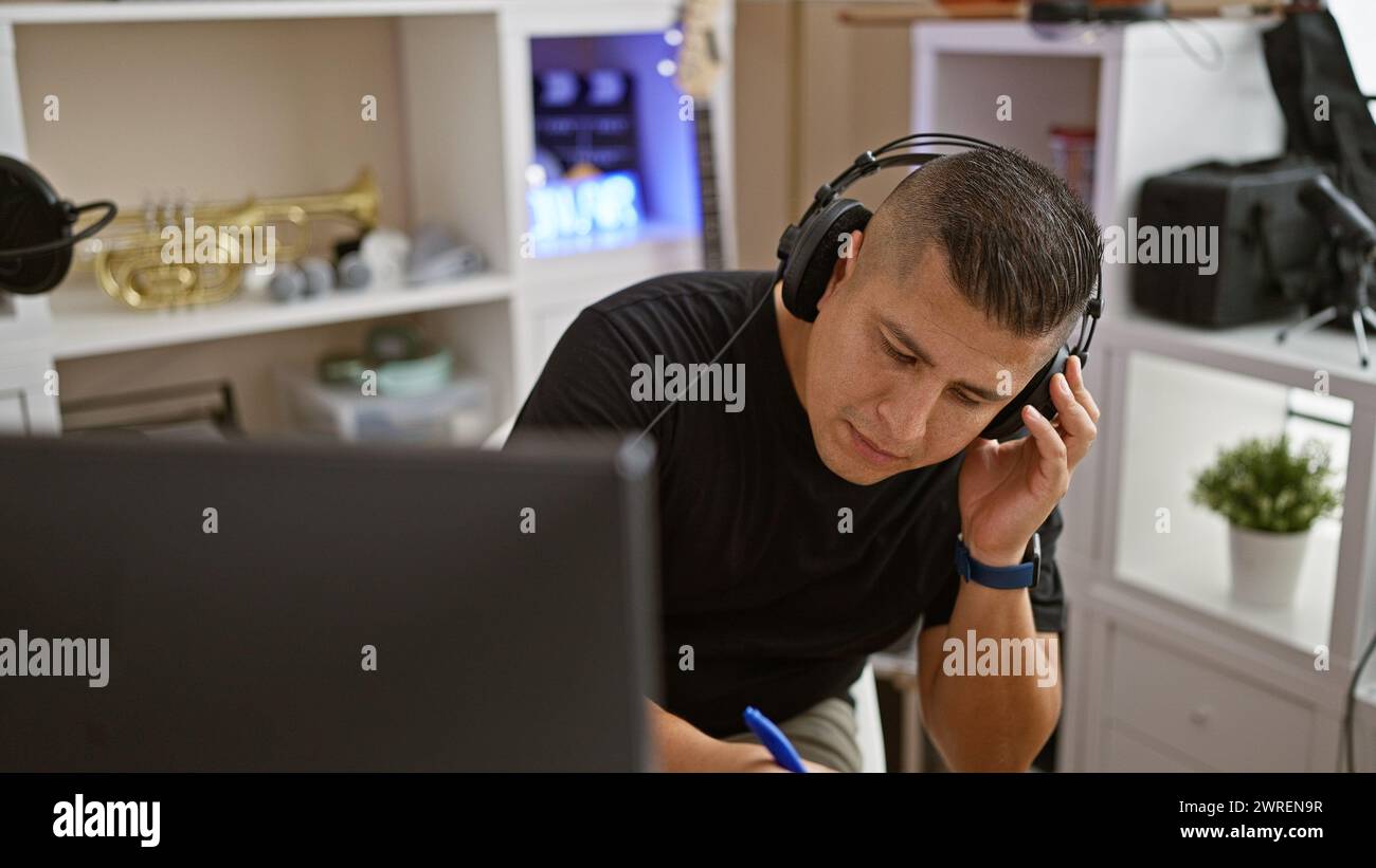 Talented young latin musician engrossed in crafting a soulful song at his cozy music studio, headphones on, effortlessly composing on his computer. Stock Photo