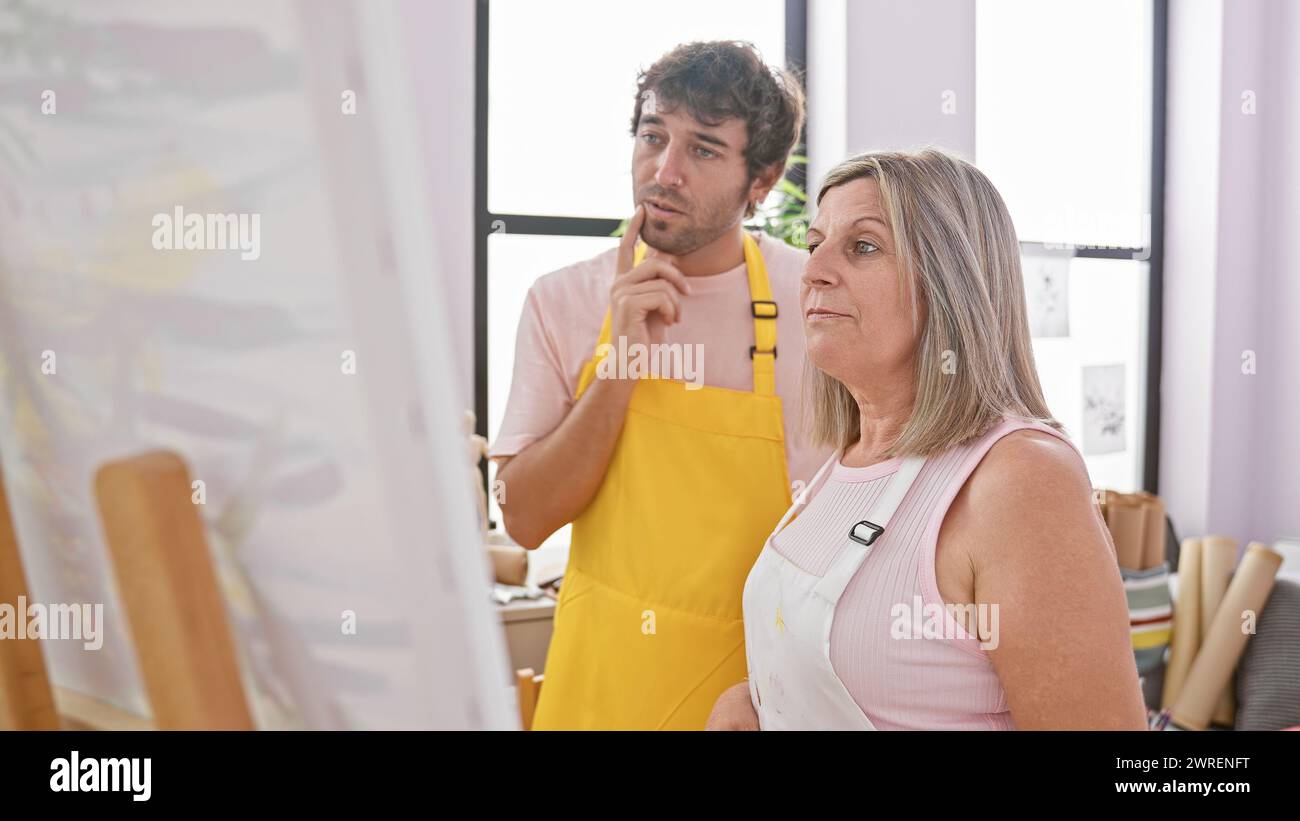 Two artists, man and woman, doubtfully ponder over a canvas, a snapshot of creativity unfolding within art studio walls Stock Photo