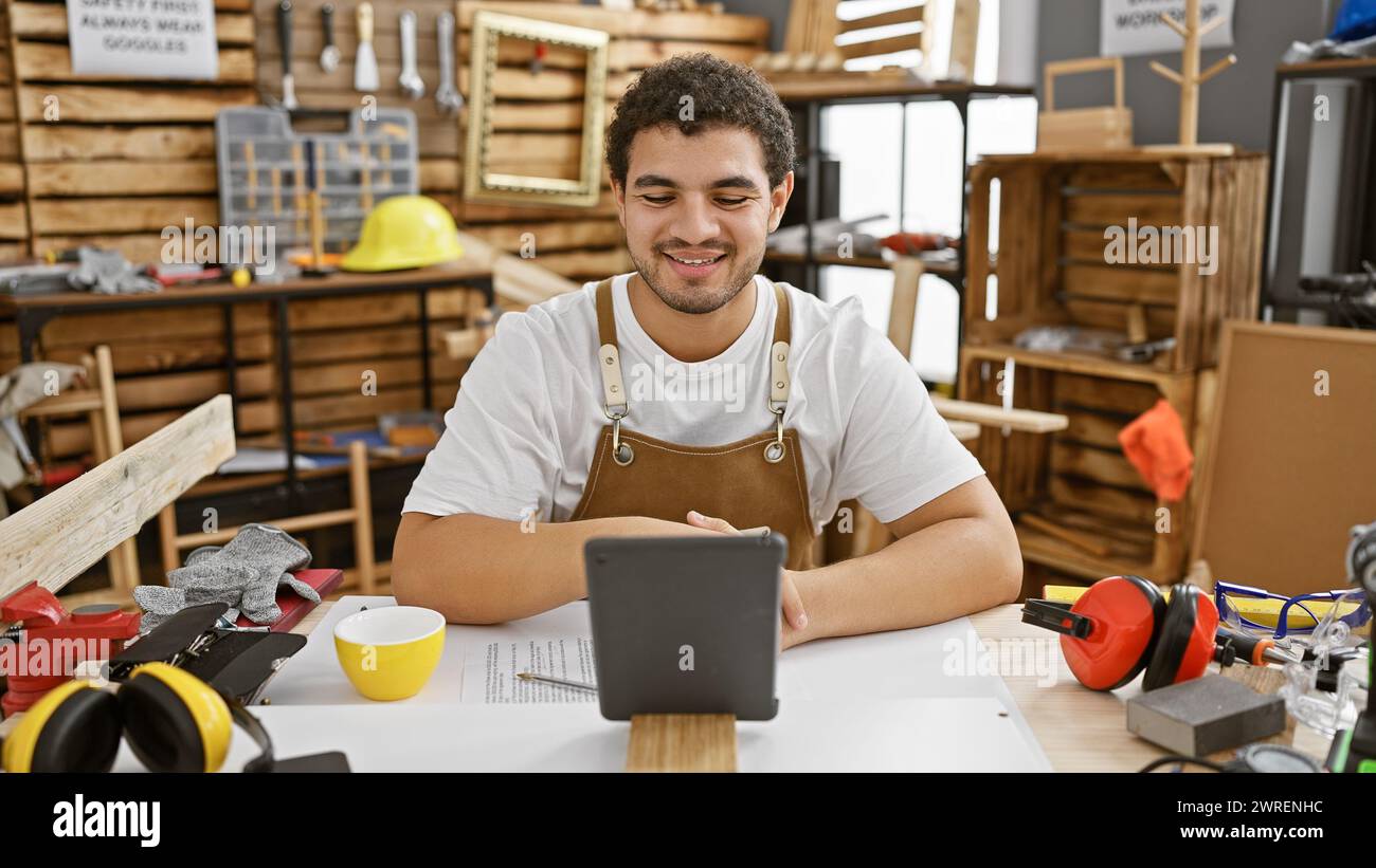 Bearded craftsman in apron using tablet in a carpentry workshop surrounded by tools Stock Photo