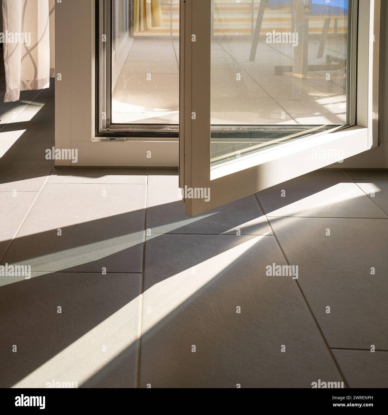 Interior with open door to the balcony and pattern of sun on the tiled floor. Stock Photo
