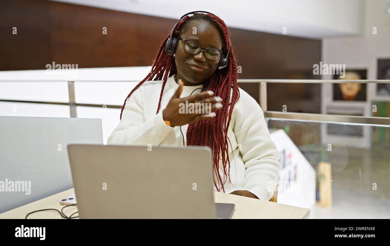Smiling african woman with braids wearing headphones at indoor office