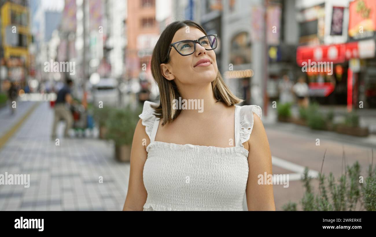 Globe-trotting beauty, stunning adult hispanic woman with glasses, looking around the vibrant tokyo cityscape. this brunette tourist is mesmerized by Stock Photo