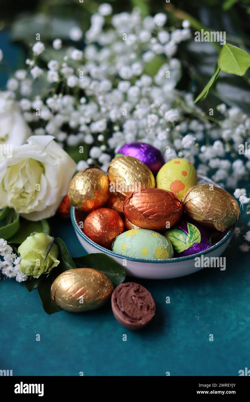 Foil wrapped Easter chocolate eggs in a glass bowl. Easter celebration concept. Colorful still life with sweets. Textured background with copy space. Stock Photo