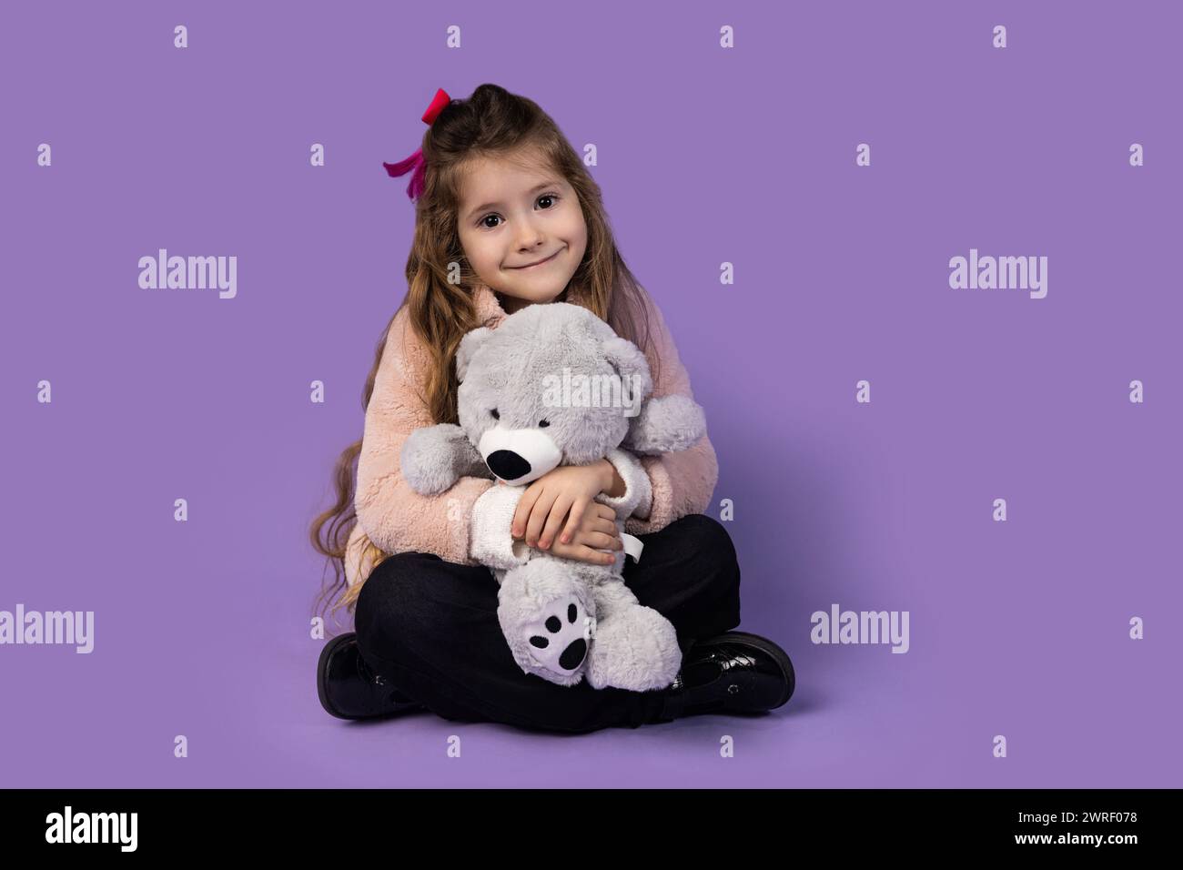 A little girl surprised as she sits with a teddy bear in her hand and holds it close to her chest because the toy is her best and closest friend. The Stock Photo