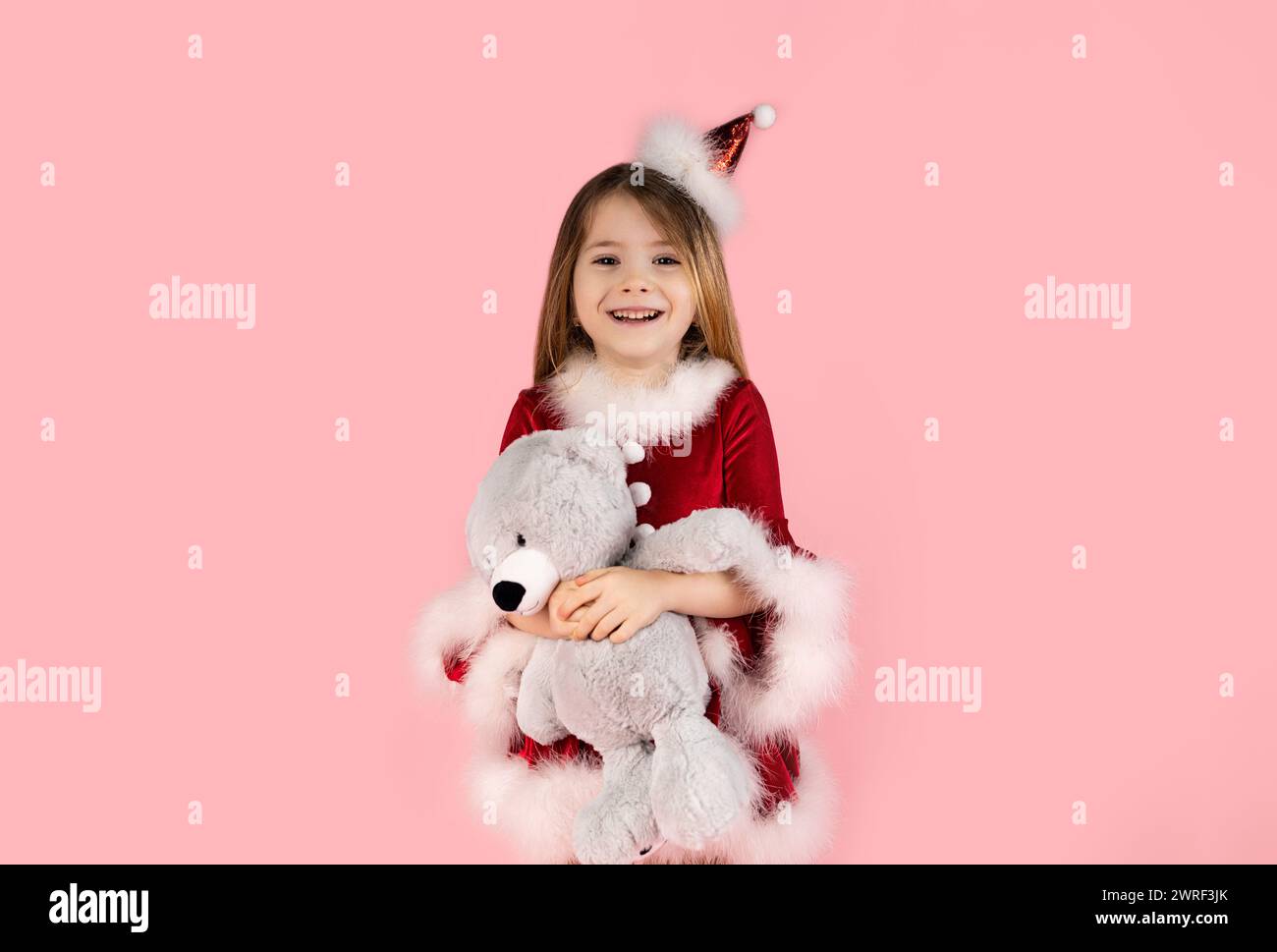 Christmas, teddy bear and happiness with a girl in studio with pink background, dressed in red Christmas dress. Bears the most wonderful Christmas gif Stock Photo