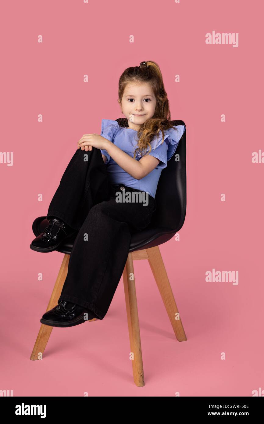 Full length shot of a stylish little girl sitting on a black chair in a ...