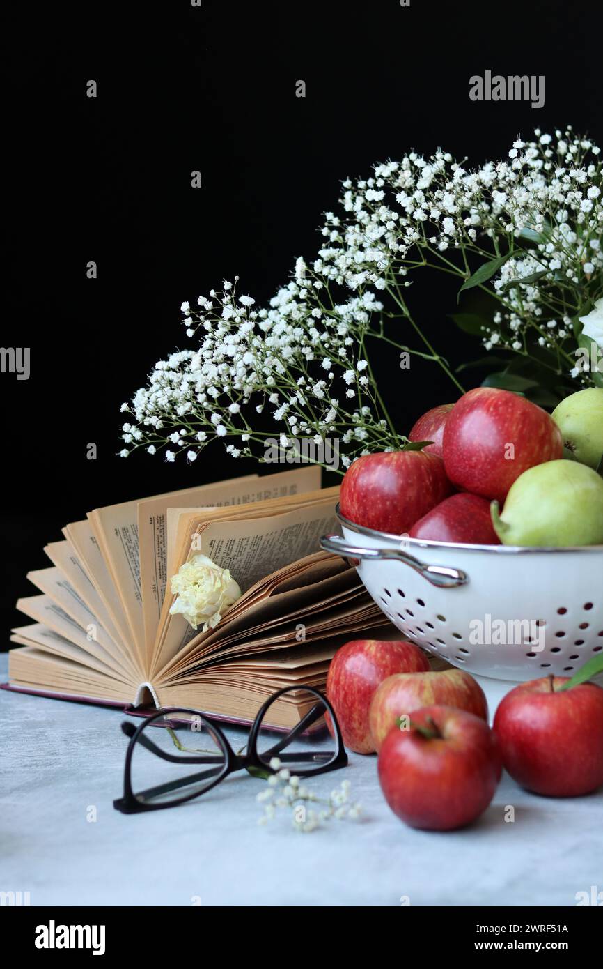 Shiny red apples, white Gypsophila flowers and open book on a table. Black background with copy space. Eating fresh concept. Stock Photo