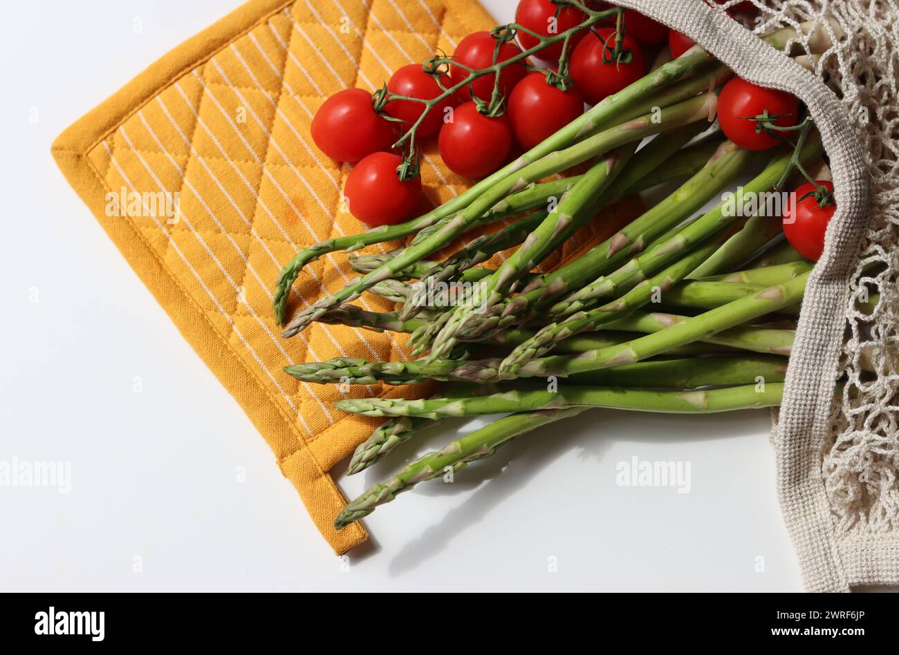 Fresh cherry tomatoes and green raw asparagus on white background with copy space. Eating fresh concept. Vegetarian meal ingredients. Stock Photo