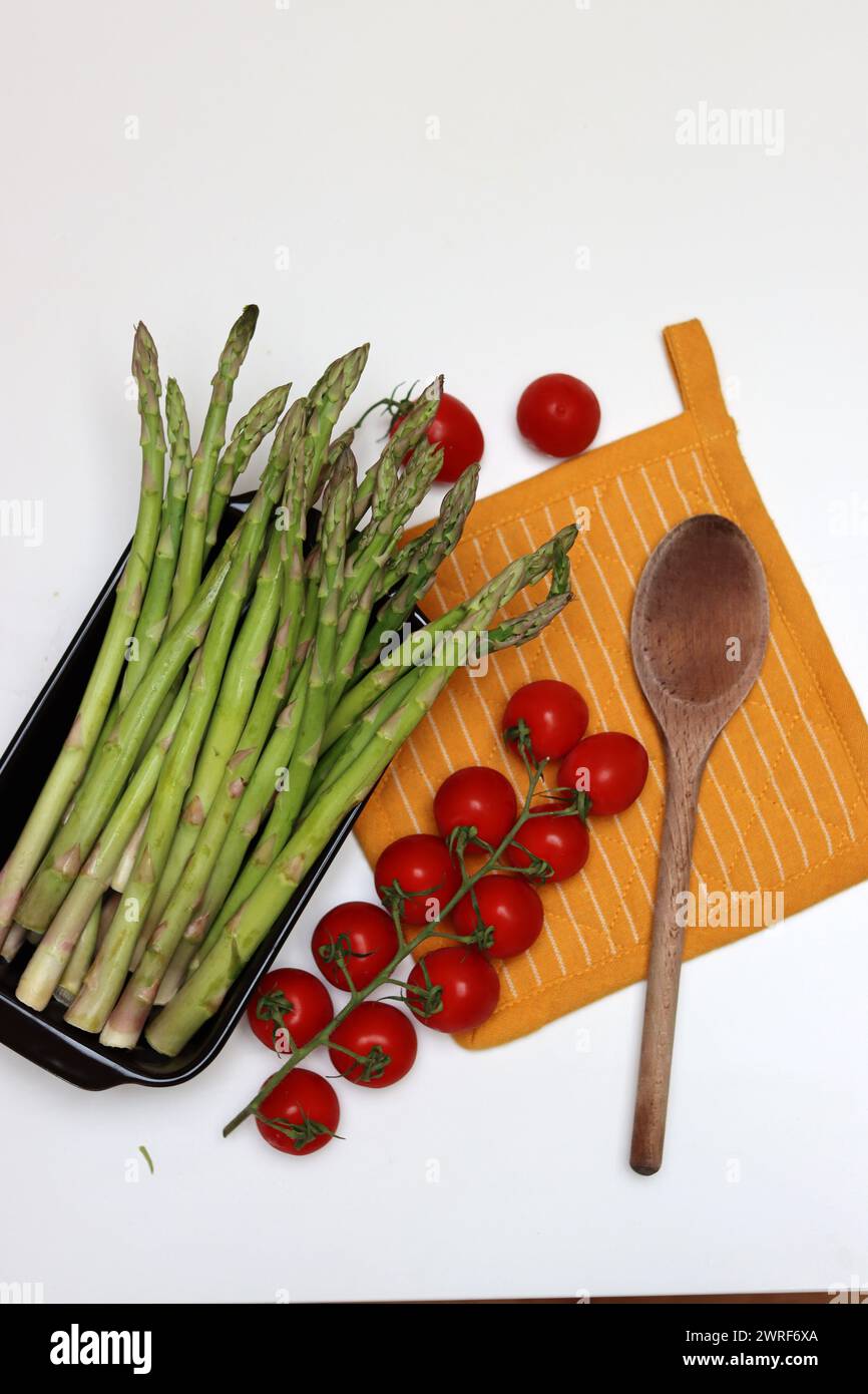 Fresh cherry tomatoes and green raw asparagus on white background with copy space. Eating fresh concept. Vegetarian meal ingredients. Stock Photo