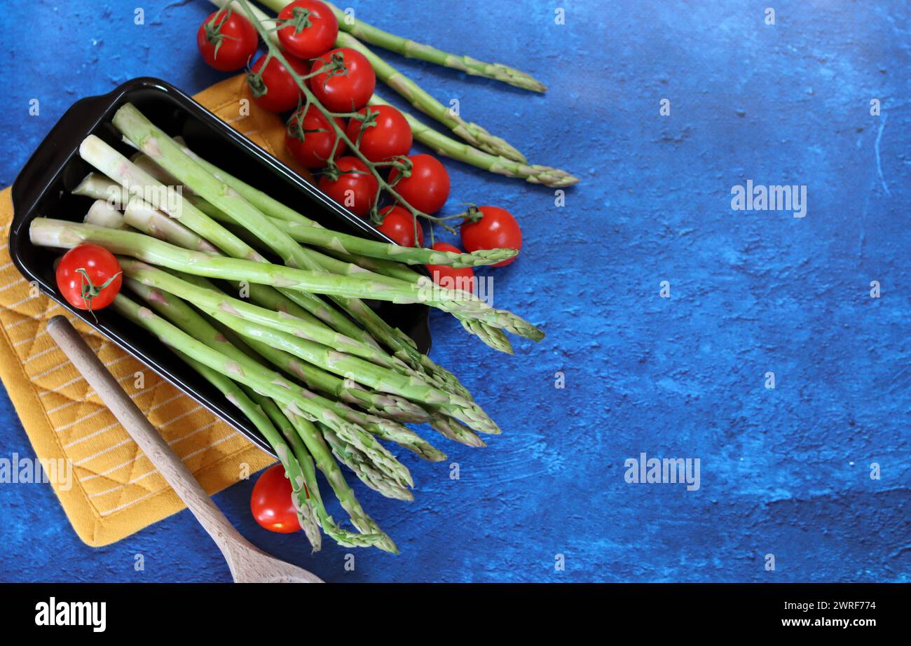 Fresh green asparagus and cherry tomatoes on blue textured background with copy space. healthy dinner preparation. Balanced diet concept. Stock Photo